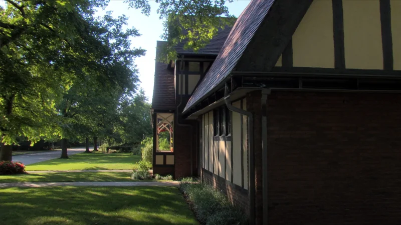 Tudor Revival home in Avondale Estates, GA under a mature oak canopy, with dark seamless gutters and downspout along the eave