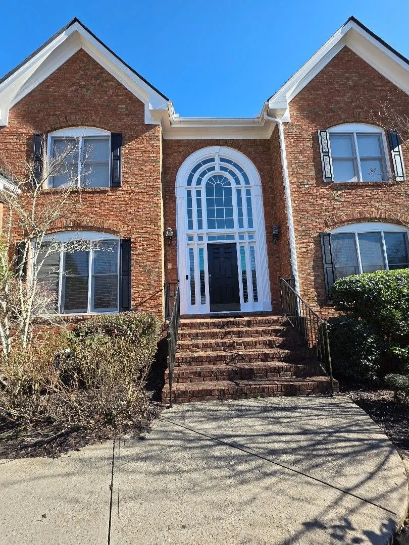 Front of a two-story red-brick home with a tall arched entry, black shutters and white gutters in Alpharetta, GA, where we upgraded the full gutter system to 6-inch
