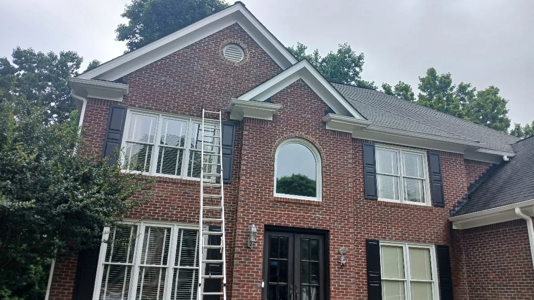 Two-story red-brick Alpharetta, GA home with white gutters and black shutters, where we replaced a damaged section of the front upper gutter