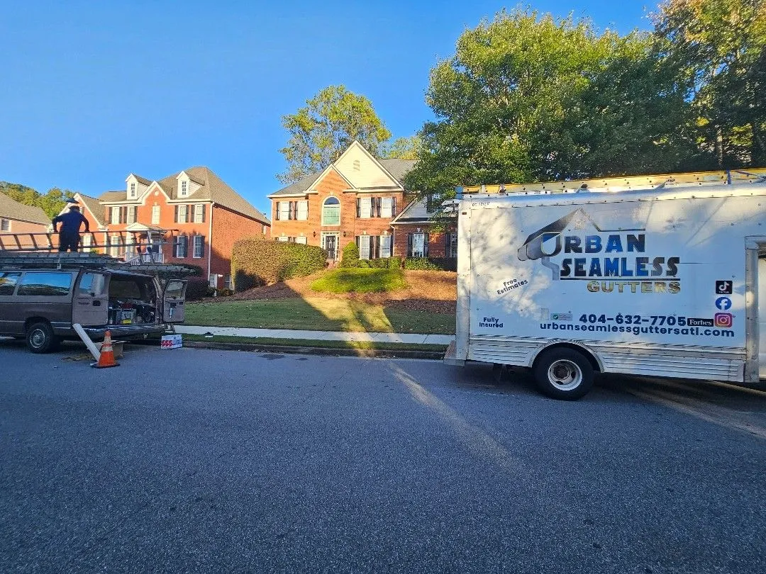 Urban Seamless Gutters truck and crew van parked outside a two-story brick home in Alpharetta, GA during a full gutter replacement