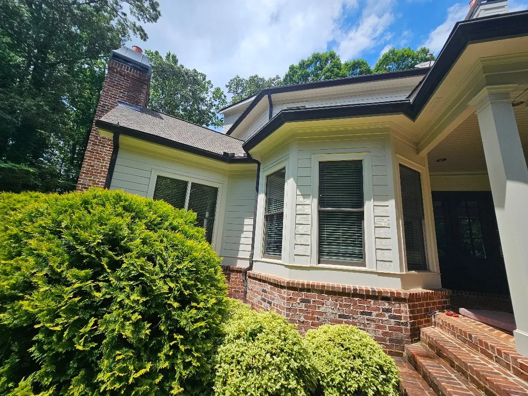 Alpharetta, GA home with light lap siding, a brick base and dark gutters, where we cleaned out and resealed a slow-draining rear gutter