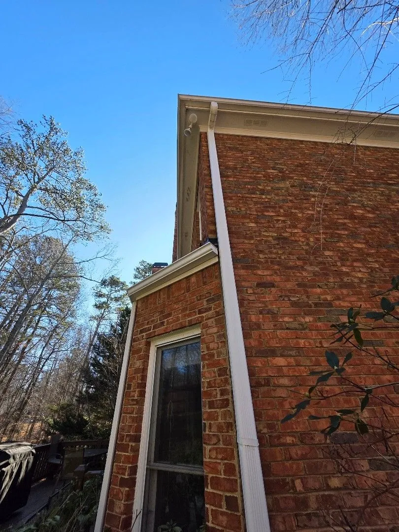 Downspout running down a brick corner from the upper gutter, beside a lower roof gutter, in Alpharetta, GA