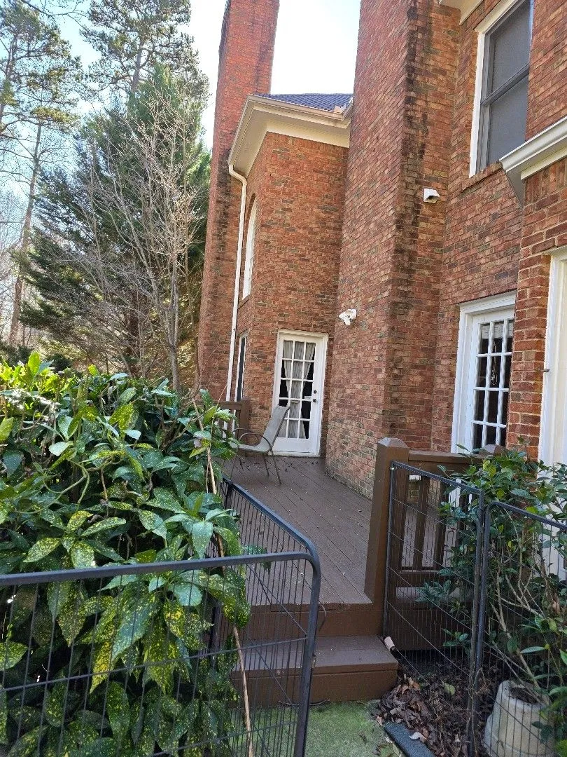 Back of the brick home with a wood deck, two tall chimneys and gutters along the rooflines, in Alpharetta, GA