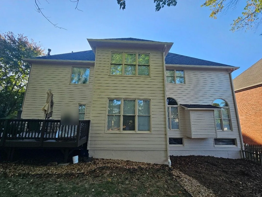 Back of the house showing the long rear rooflines with gutters and downspouts over cream siding, in Alpharetta, GA