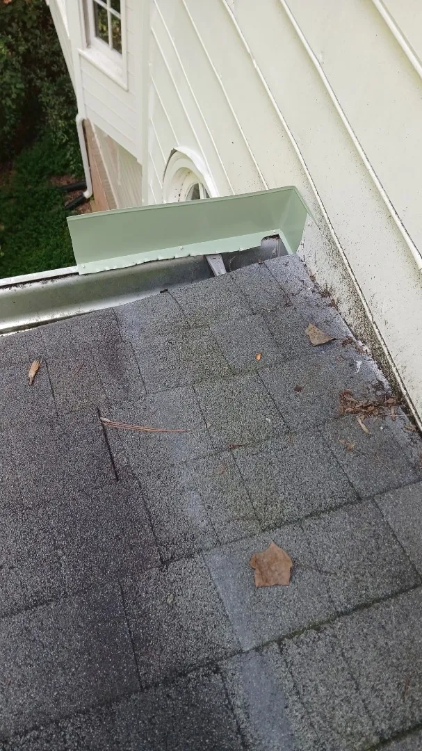 Gutter along the edge of a lower roof where it meets light lap siding, with an old splash guard at the corner by the wall, seen from above on an Alpharetta, GA home