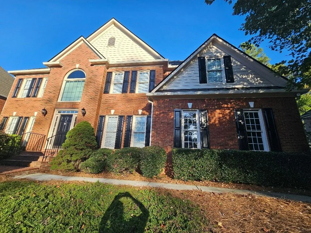 Front of a two-story red-brick home with cream siding gables and black shutters in Alpharetta, GA, where we replaced the full gutter system