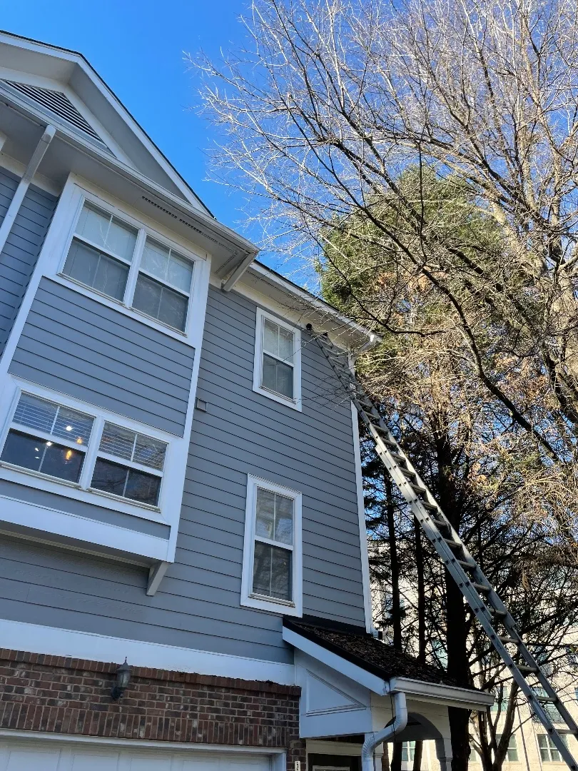 Three-story gray townhome with white trim and a brick garage level, an extension ladder reaching the roofline, at a townhome community in Atlanta, GA