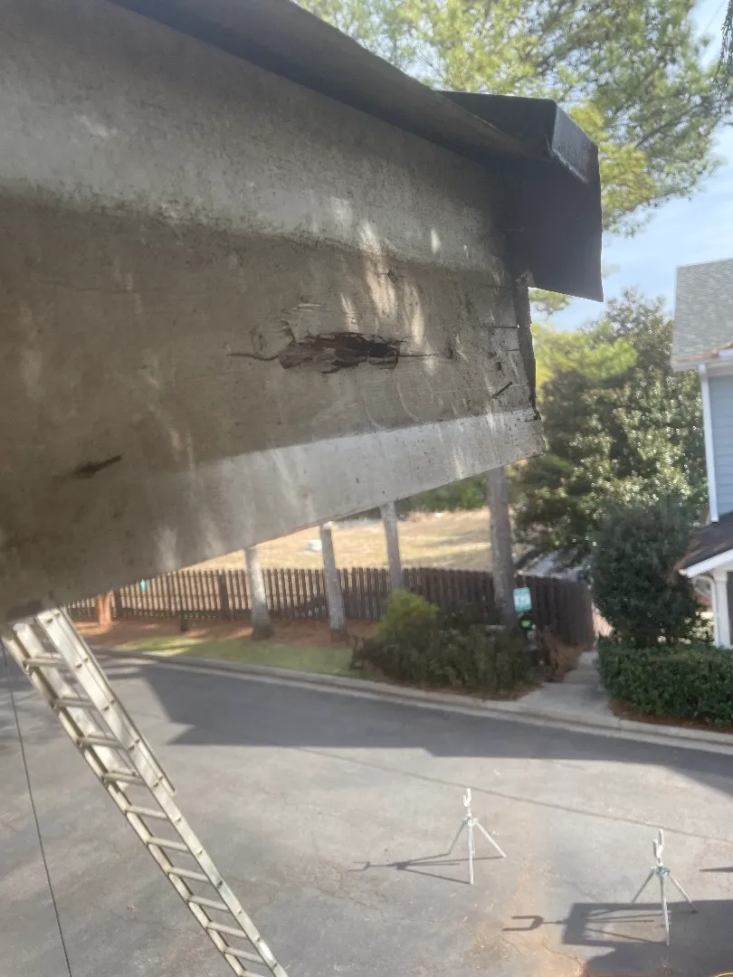 Before: rot splitting a fascia board under a metal roof edge at an Atlanta, GA townhome, with the gutter off and the parking court below