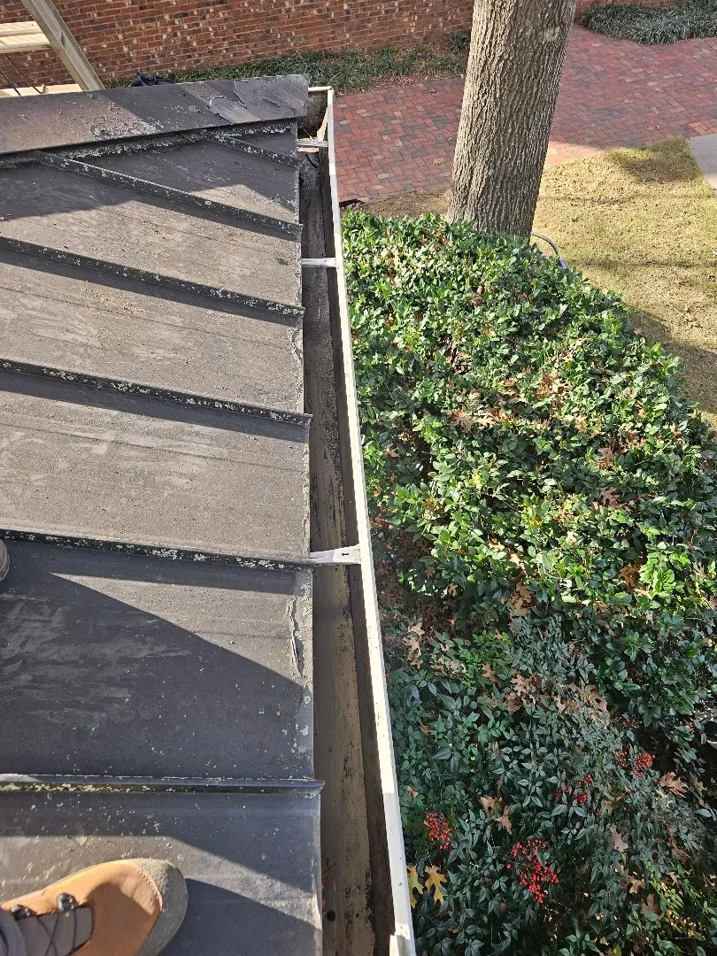 White gutter with hidden hangers along a dark metal roof edge, with a hedge, a tree and a brick walkway below, at a townhome community in Atlanta, GA