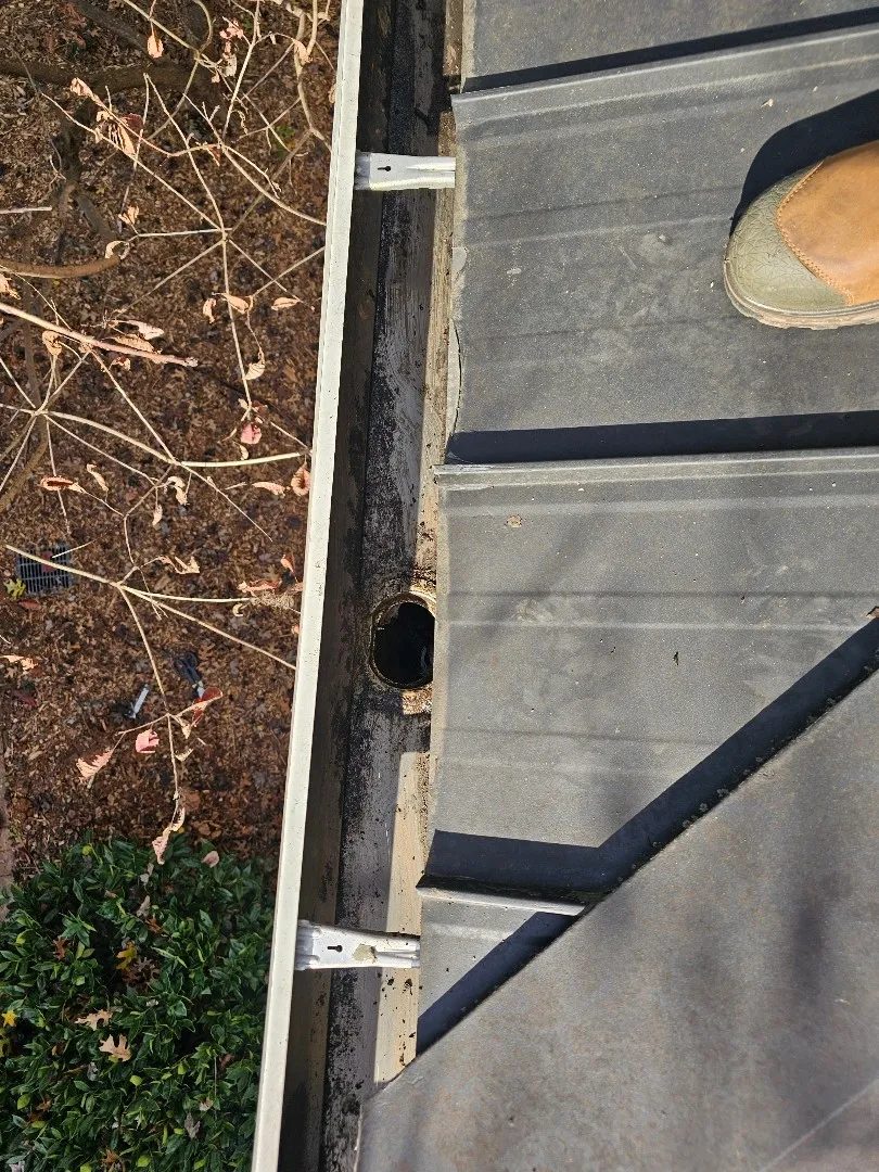 Inside a gutter on a metal porch roof: an open downspout outlet hole between two hidden hangers, at an Atlanta, GA townhome
