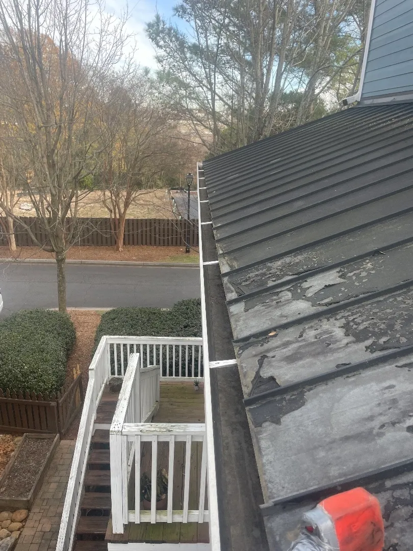 Gutter along a standing-seam metal roof with peeling paint, above a townhome’s deck stairs and the street, in Atlanta, GA