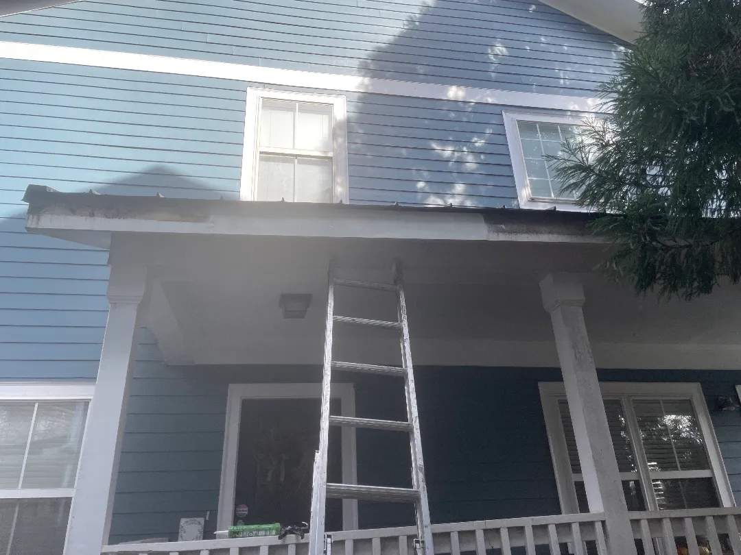 Two-story blue townhome in Atlanta, GA with a ladder against the front porch roof and the old gutter off the roof edge