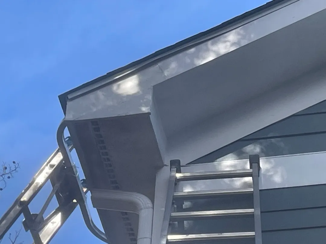 Roof corner of a gray townhome in Atlanta, GA, seen from below, with a white downspout elbow and two ladders