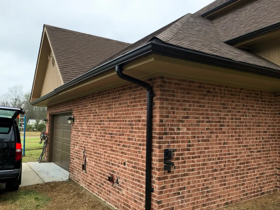 Continuous black seamless gutter runs with color-matched downspouts on a brick Lithonia, GA home