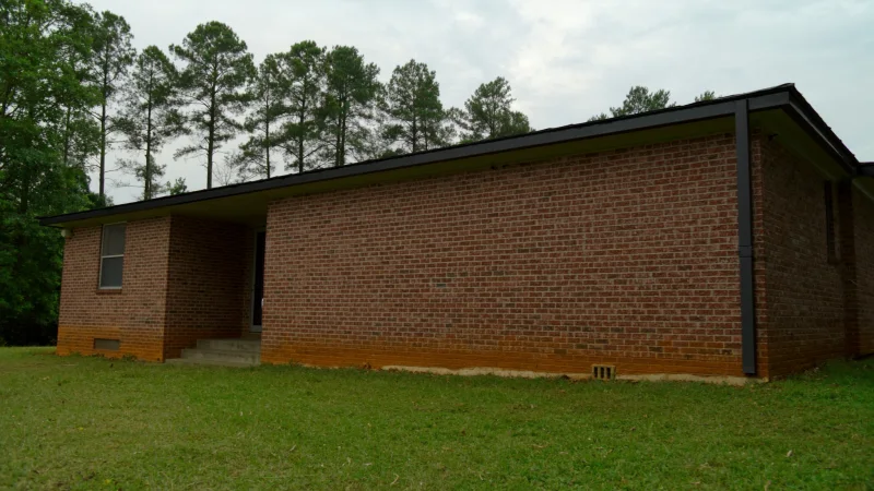Brick ranch home in McDonough, GA backed by Georgia pines, with black seamless gutters along the roofline in Henry County